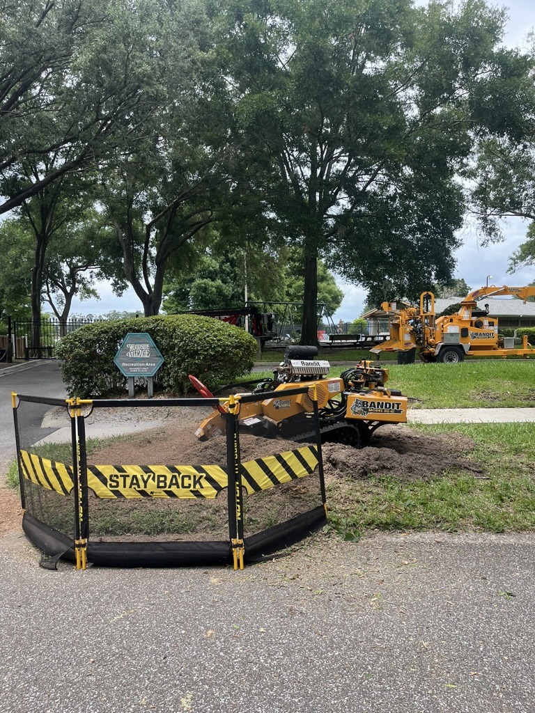 A maintenance machine working in a park, surrounded by safety barriers. Signage indicates a recreation area. Trees and greenery fill the background.