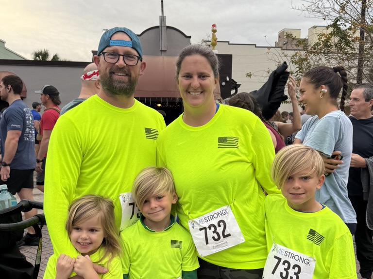 A group of five individuals wearing matching neon shirts and participating in an outdoor event with others around. No landmarks are visible.