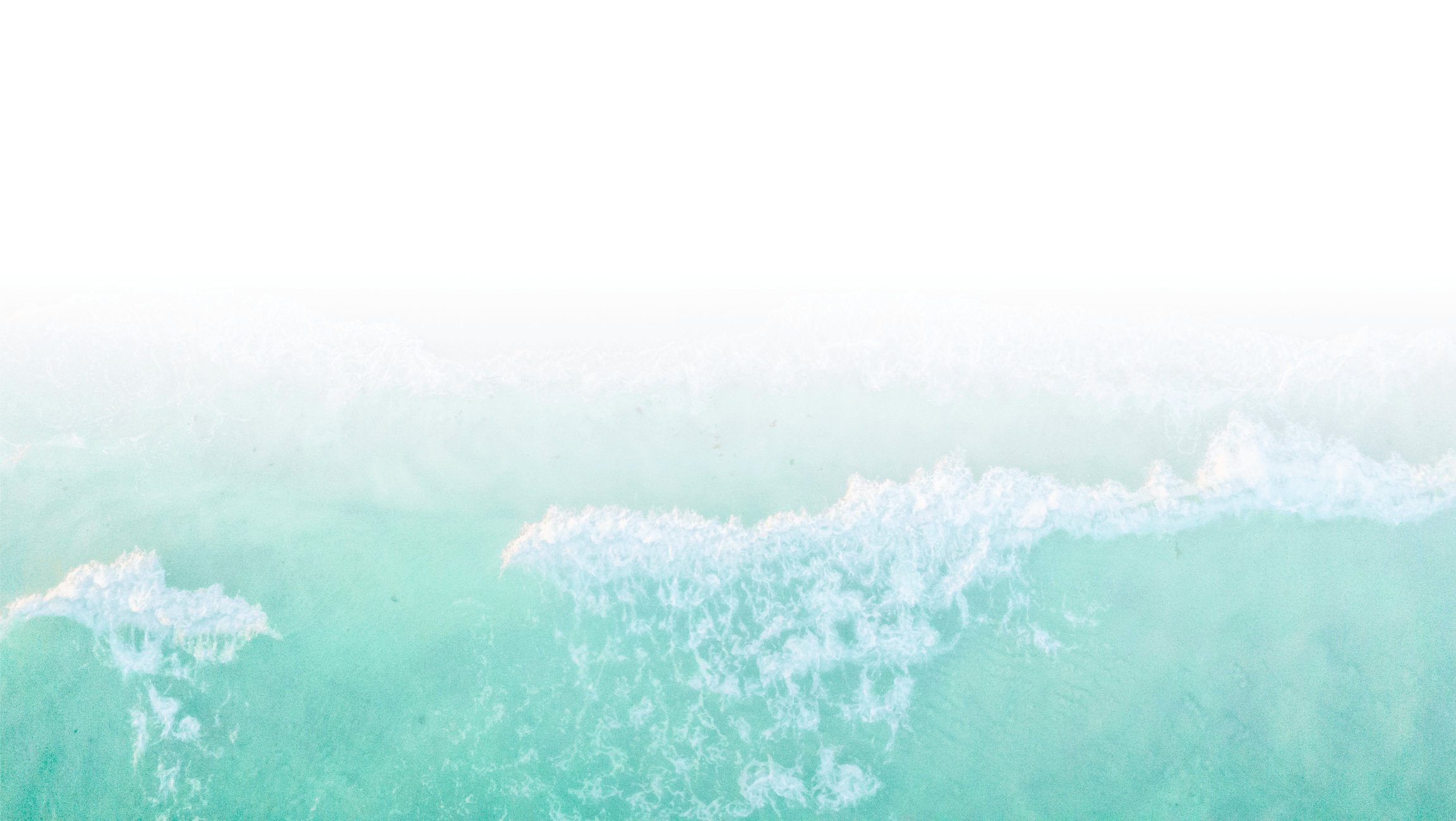 Aerial view of turquoise ocean waves gently breaking onto the shore, creating a calming, serene coastal scene with an overexposed sky.